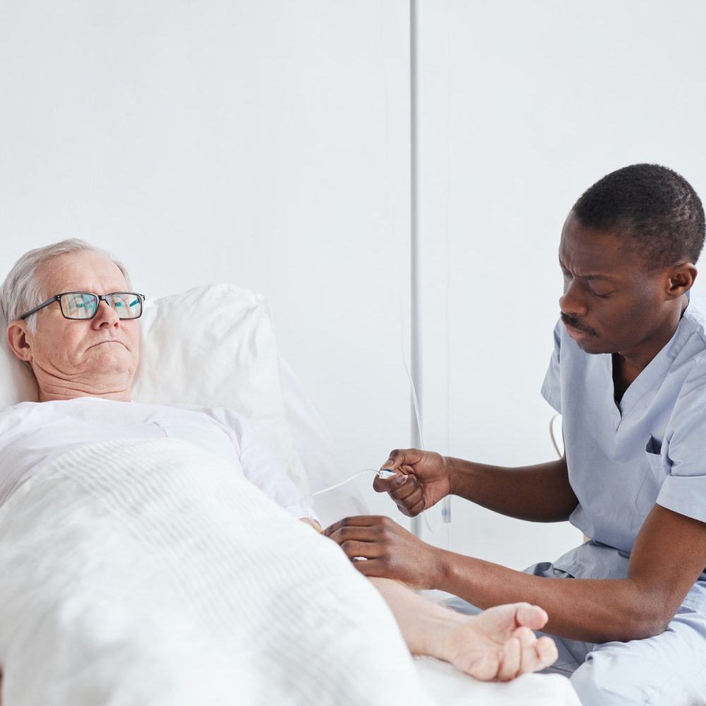 A male nurse cares for an elderly person inside his house.