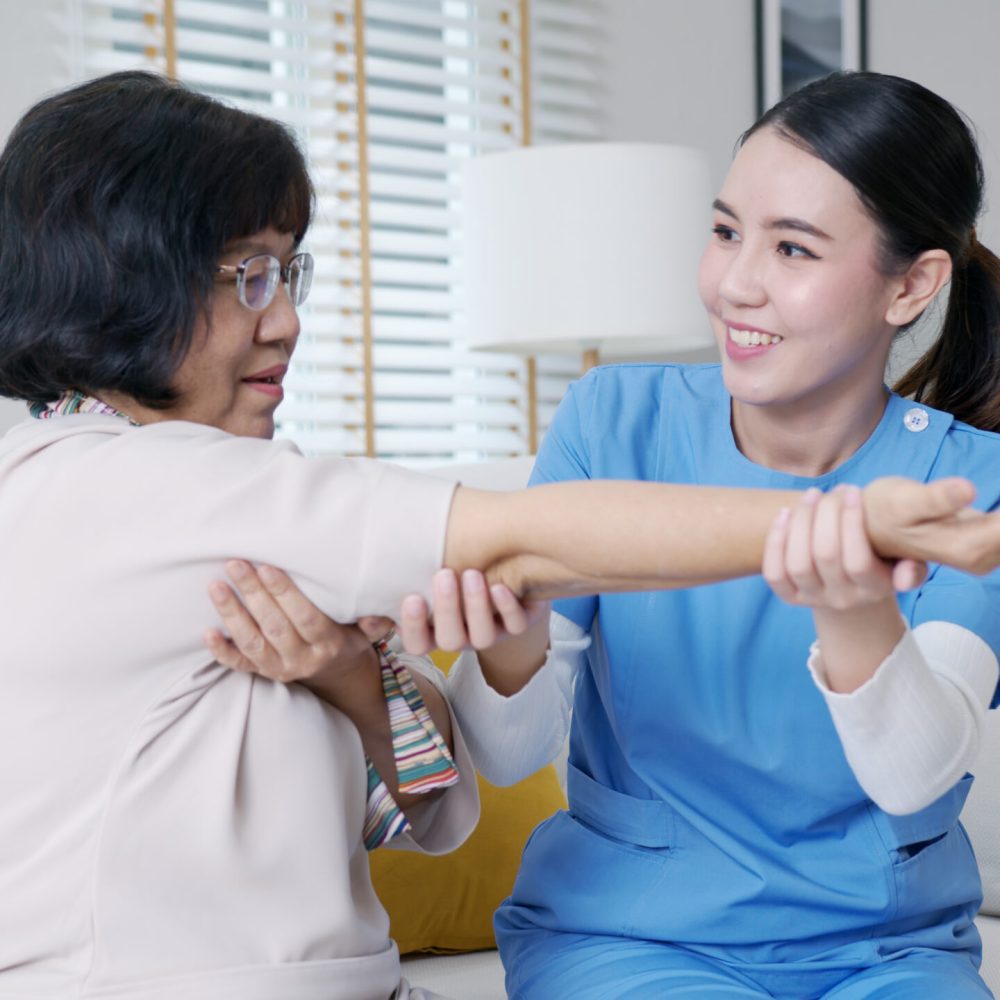 A young Asian home health nurse gives physiotherapy to an aging senior at home.